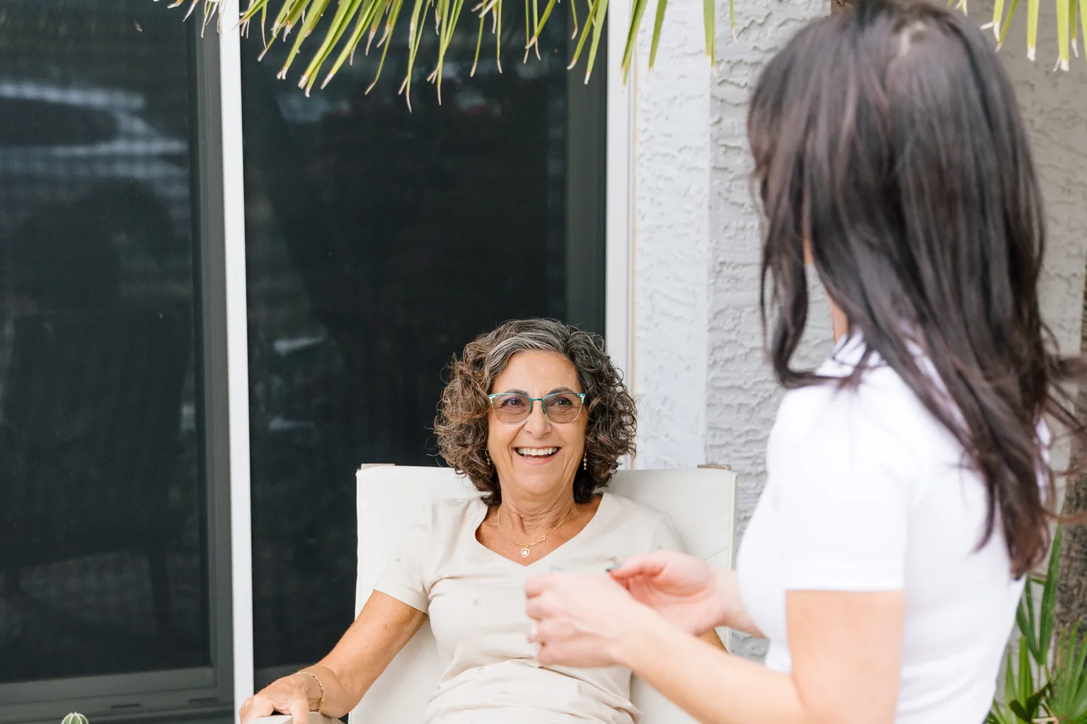 Prata Health registered nurse at the side of a smiling older client resting in her patio chair at home