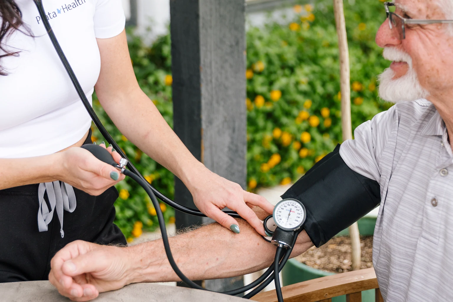 Prata Health registered nurse checking an older client's blood pressure with a manual cuff and stethoscope