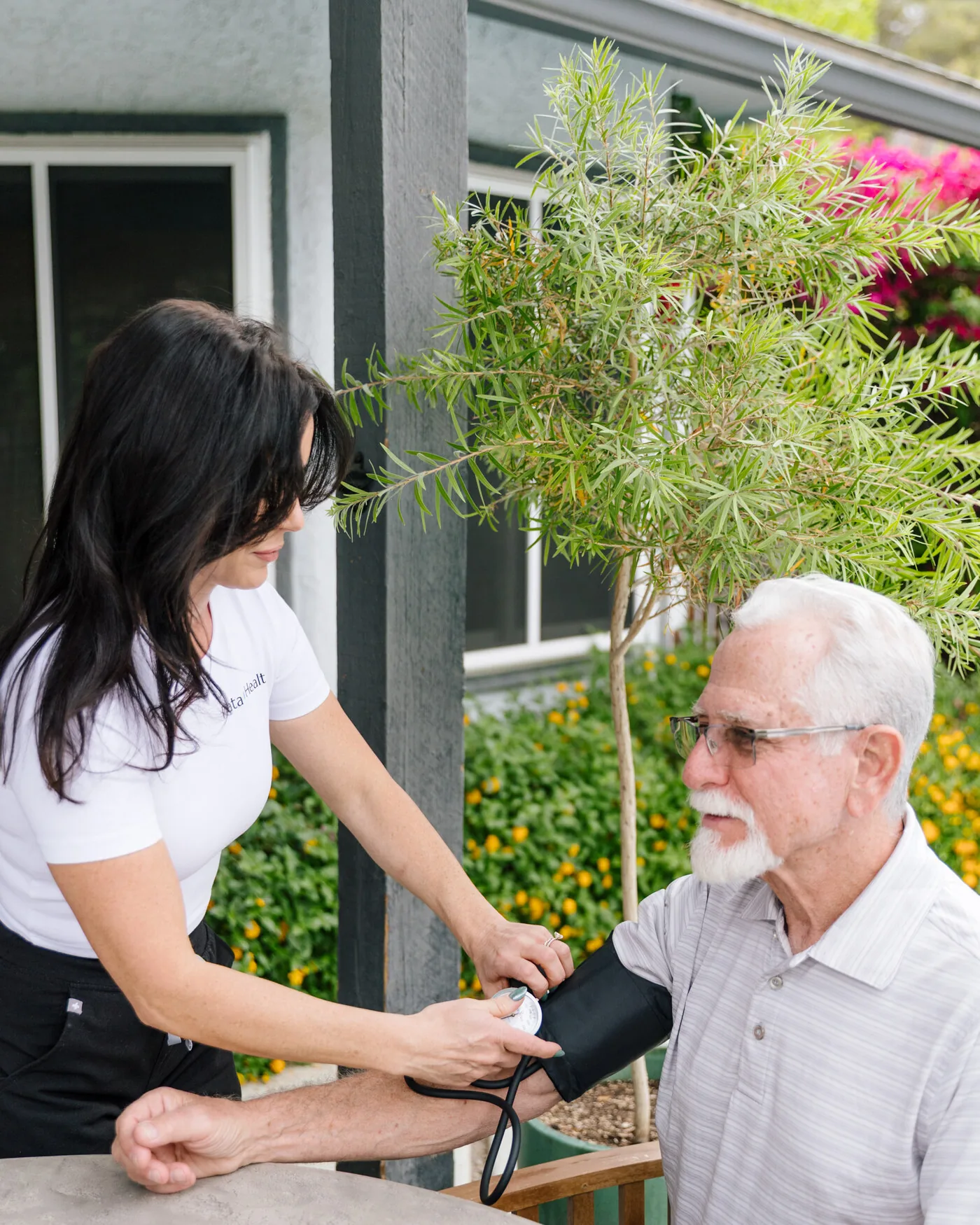 A Prata Health nurse taking an older client's blood pressure at a patio table
